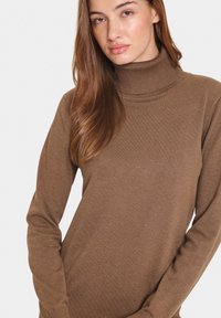 Maglione a collo alto marrone in texture a coste, con maniche lunghe e forma aderente, dotato di un colletto alto. Design semplice.