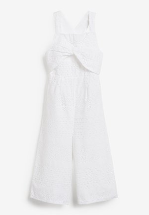 Combinaison blanche à jambes larges, réalisée en tissu texturé avec un motif découpé. Comprend un détail torsadé à l'avant et des bretelles ajustables.