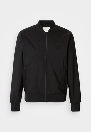 Must musternahk, mis on valmistatud siledast kangast, esiosa lukuga, kahe küljetaskuga, soonikustega varrukates ja ümmarguse kaelusega. Muster puudub.