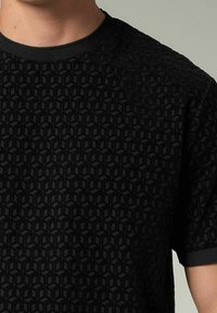 Camiseta negra con un patrón geométrico texturizado que presenta cubos en relieve. Cuello de canalé y mangas cortas. Acabado de tela suave.