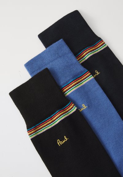 Tre paia di calze: una nera con un bordo superiore a strisce colorate, una blu e un'altra nera con ricamo dorato che scrive "Paul".