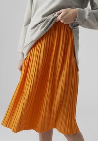 Plisserad kjol i klar orange färg, gjord av texturerat tyg. Visar vertikala veck med en flytande design, kombinerad med en grå lång�ärmad topp.