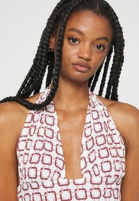 Vestido com decote halter, apresentando um padrão geométrico em vermelho sobre um fundo branco, com um decote profundo e tecido franzido na cintura.