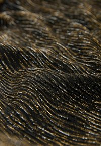 Schwarzer und goldener Textilstoff mit metallischen Fäden, die in gewellten Mustern angeordnet sind und das Licht für einen schimmernden Effekt reflektieren.