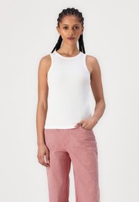 Weißes, geripptes Tanktop mit rundem Ausschnitt, tailliertem Schnitt und ärmelloser Ausführung. Kombiniert mit gestreiften, rot-weißen weiten Hosen.