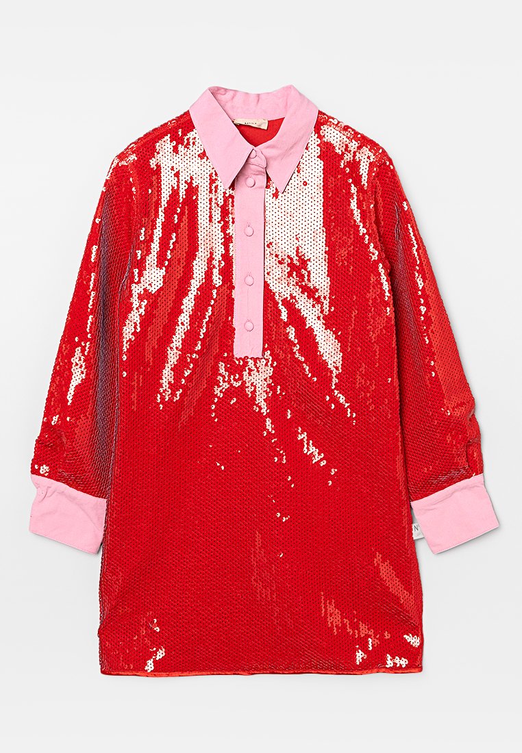 Maglietta rossa con paillettes e colletto rosa, con una patta dei bottoni, maniche lunghe con polsini rosa e una texture lucida.
