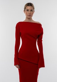 Completo a due pezzi rosso a coste, composto da un top off-shoulder con maniche lunghe e una gonna aderente con orlo asimmetrico.