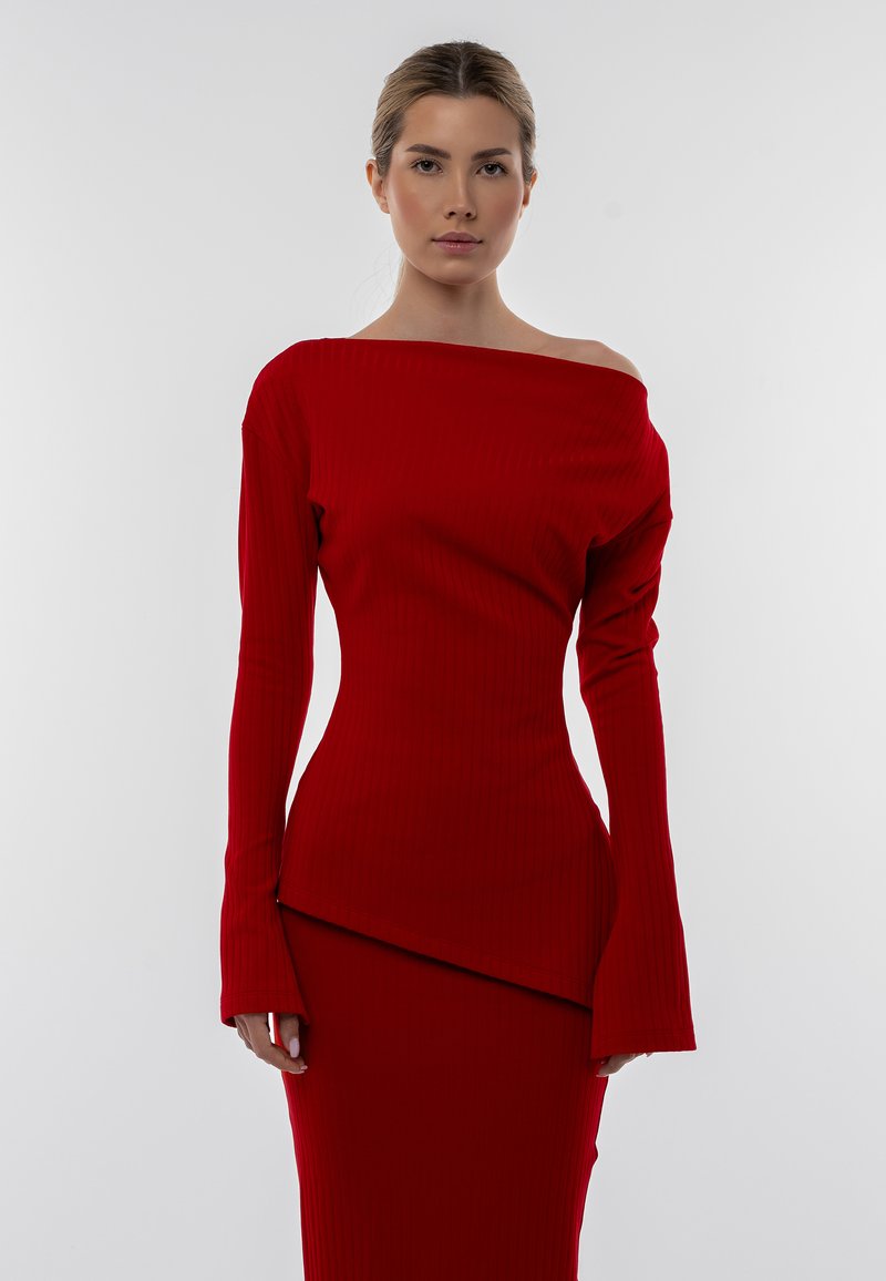 Completo a due pezzi rosso a coste, composto da un top off-shoulder con maniche lunghe e una gonna aderente con orlo asimmetrico.