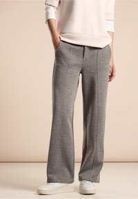 Šedé kostkované kalhoty s volným střihem, vysokým pasem a bočními kapsami. V kombinaci s bílými teniskami, které mají texturovanou tkaninu.