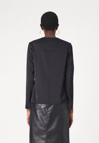 Haut noir à manches longues avec une silhouette droite et un détail de couture minimal, associé à une jupe en cuir noire taille haute.
