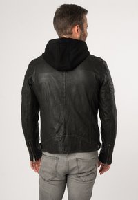 Schwarze Lederjacke mit schwarzem Kapuzen, strukturiertem Finish, Reißverschlussmanschetten und taillierter Passform. Getragen über grauen Jeans.