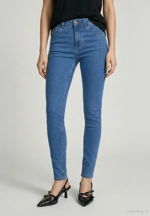 Niebieskie dżinsy o wąskim kroju noszone z czarnymi szpilkami ze zgiętym noskiem i czarnym topem, obciętym na wysokości talii.