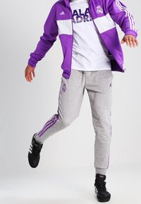 Lila träningsjacka med vita detaljer, grå sweatpants med lila ränder och svarta sportskor. Enkel vit T-shirt under.