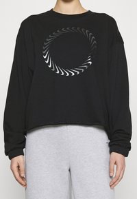 Svart kort sweatshirt med en rund silvrig grafisk design. Tyget ser mjukt ut med ribbade manschetter och en avslappnad passform.