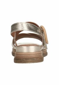 Sandali in pelle dorata metallizzata con retro aperto, cinturini incrociati e un tacco in legno con texture naturale. Presentano una fibbia rotonda di colore chiaro.