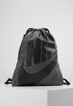 Szary plecak Nike z troczkami, z dużym czarnym logo Nike, umieszczony na białej powierzchni na tle jednolitego jasnoszarego tła.