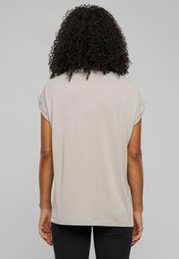 Ljusbeige kortärmad topp med uppvikta ärmar, avslappnad passform och mjuk textur, kombinerad med svarta leggings. Minimalistisk design.