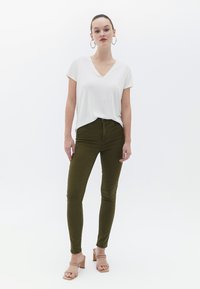 Maglietta bianca a scollo a v, pantaloni skinny verde oliva e sandali con tacco a blocco beige. Design semplice, texture liscia, silhouette aderente.