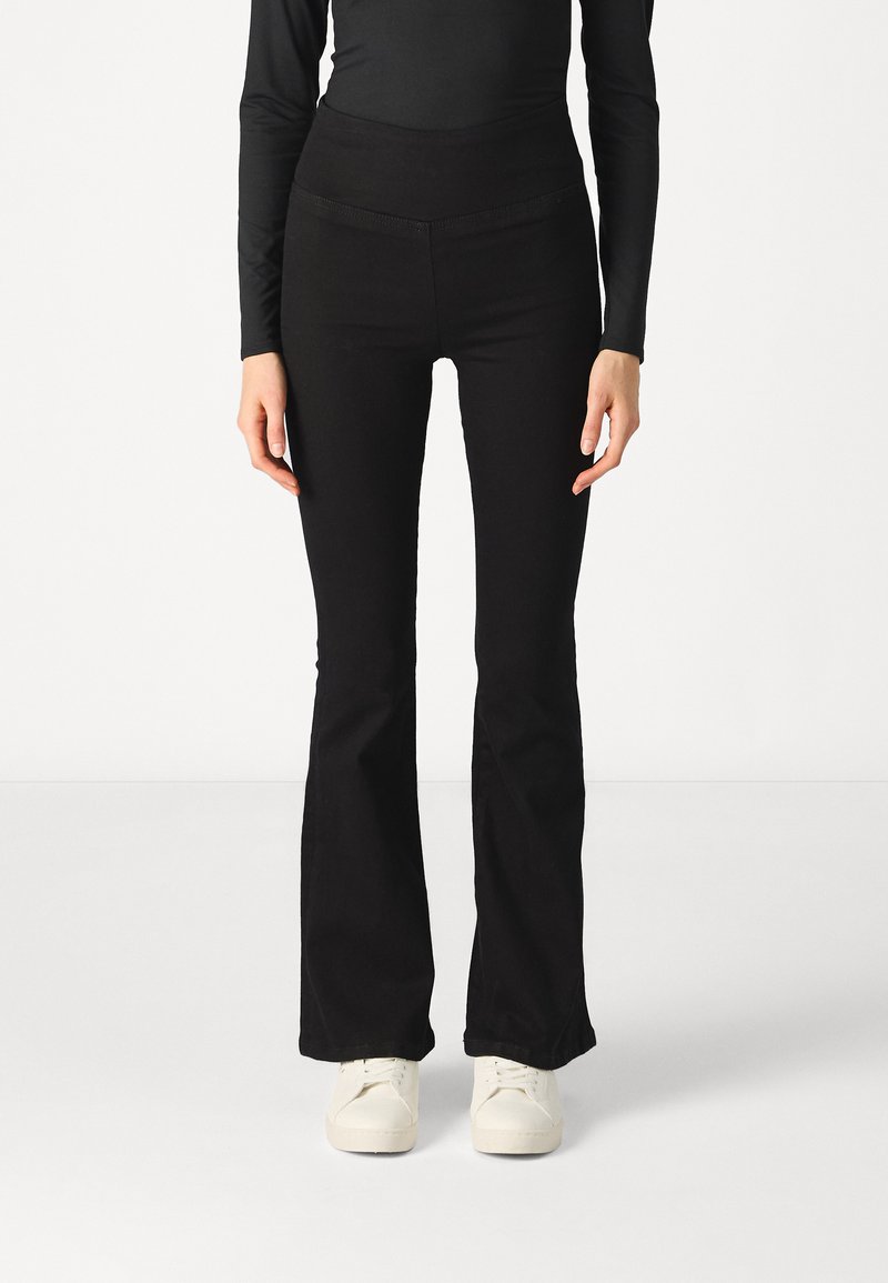 Black flared pants feature a stretchy, smooth fabric with a high waistband. Paired with white sneakers for a contrasting look.