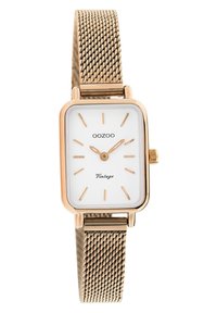 Montre carrée dorée avec un cadran blanc, des marqueurs d'heure minimalistes, un bracelet en maille métallique et une petite couronne sur le côté pour les réglages.