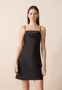 Robe nuisette en satin noir avec des bretelles spaghetti et un col bordé de dentelle. Texture lisse, design à mi-genoux, style minimaliste.