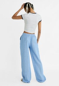 Jasnoszary krótki t-shirt z ciemnoniebieskimi wykończeniami, w połączeniu z niebieskimi spodniami o szerokich nogawkach, z elastycznym pasem i kieszeniami bocznymi.