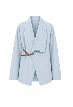 Femme portant une veste oversize bleu clair avec une boucle marron, une chemise blanche, un jean à jambes larges, des talons plateformes noirs et tenant un sac à main tissé.
