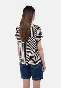 Haut à manches courtes beige avec des rayures diagonales noires ; coupe décontractée ; associé à un short en denim bleu ; design simple et tissu texturé.