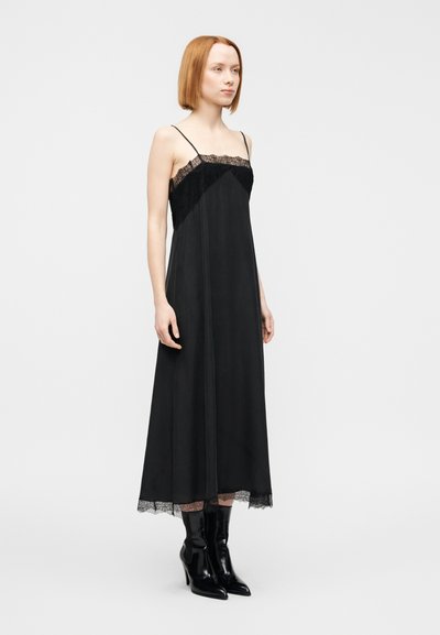 Μαύ ρο φόρεμα με δαντέλα στο ντεκολτέ και στο τελείωμα, λεπτές τιράντες, σχήμα Α, λείο ύφασμα, συνδυασμένο με μαύρα μποτάκια με τακούνι.