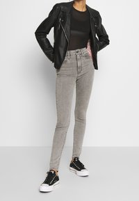 Jeans grises ajustados de cintura alta con un acabado texturizado, combinados con una chaqueta de cuero negra y zapatillas negras con suelas blancas.