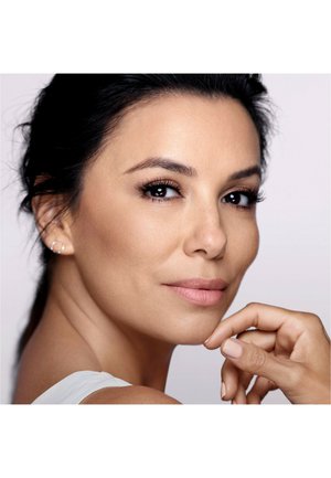 Gros plan du visage d'une femme aux cheveux noirs, à la peau lisse, avec un maquillage subtil et des lèvres naturelles. Elle porte une boucle d'oreille et repose son menton sur sa main.