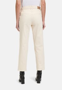 Kremowe spodnie z prostymi nogawkami, z wysokim stanem, tylnymi kieszeniami i subtelną fakturą na dolnym brzegu, zestawione z czarnymi botkami.
