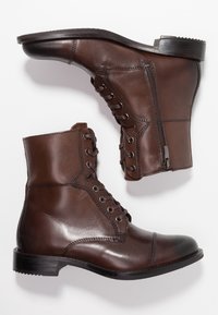 Botas de cuero marrón hasta el tobillo con un acabado suave, cordones en la parte delantera, cremallera lateral, punta redonda y tacón bajo apilado.