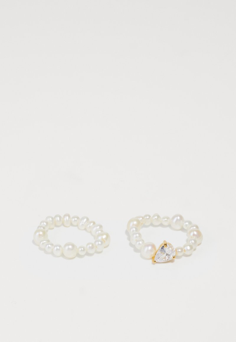 Two rings made of small white pearls; one features a gold-setting pear-shaped crystal accent. The other is a full pearl band.