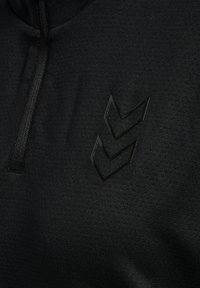 Suéter negro con media cremallera, que presenta una tela texturizada y un logotipo negro brillante en forma de chevrón en el lado izquierdo del pecho.