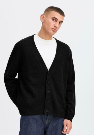 Svart strikket cardigan med V-hals, lange ermer og seks knapper foran. Stoffet virker mykt og teksturert, egnet for lagpå layering.