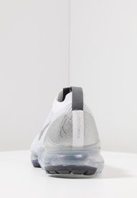 Tenisky VaporMax s pleteným bílým svrškem, šedými akcenty, transparentní podrážkou s vzduchovým polstrem a texturovaným detailem na patě.