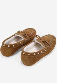 Braune Wildleder-Mokassinslipper mit weißem Futter aus Fell, silbernen Nietenakzenten entlang der oberen Kante und einem Schnürband-Detail an der Vorderseite.