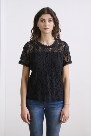 Schwarzes Spitzentop mit gewelltem Ausschnitt und kurzen Ärmeln, mit floralem Muster und kontrastierender Unterlage, kombiniert mit blauen Jeans.