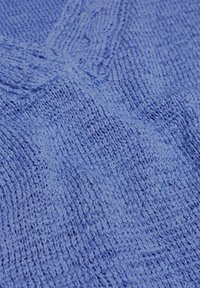 Gebreide stof in lichtblauw, getextureerd met een ribbelpatroon. Het materiaal lijkt zacht, met oneffen steken die een gezellige uitstraling geven.