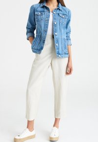 Jeansjacka i ljusblått med knäppning fram, två bröstfickor och uppvikta ärmar. Matchad med krämfärgade, löst sittande byxor och vita sneakers.