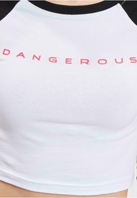 Top scurt alb cu mâneci raglan negre, având un text îndrăzneț roșu care scrie "DANGEROUS" pe piept, fabricat dintr-un material elastic din bumbac.