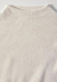 Cremefarbener gerippter Strickstoff mit vertikalen Streifen und hohem Kragen. Die Textur wirkt weich und dehnbar, geeignet für eng anliegende Kleidung.