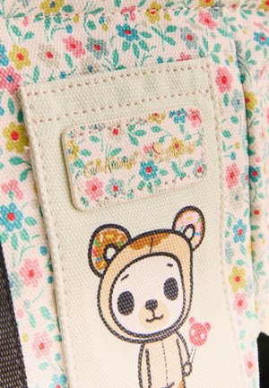 Beige blomstret stof med et påsyet mærke, hvor der står "Cath Kidston x tokidoki", og en tegneserbamse, der holder en hjerteformet slikkepind.