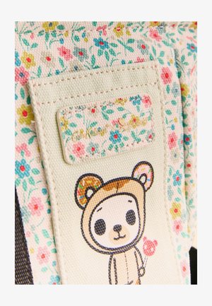 Smėlinės spalvos gėlių rašto audinys su siūta etikete, kurioje parašyta „Cath Kidston x tokidoki“ ir animacinis meškinas, laikantis širdies formos ledinuką ant pagaliuko.