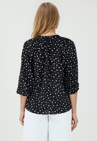 Blusa nera con pois bianchi, con scollatura arricciata e maniche a tre quarti. Realizzata in tessuto leggero, offre una vestibilità comoda.