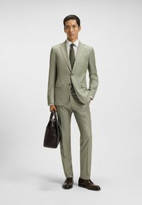 Jasnozielony garnitur o delikatnej fakturze, dopasowany krój, w połączeniu z białą koszulą i zieloną muchą w kropki. Czarne skórzane buty i ciemna torba.