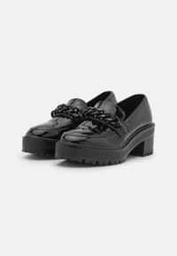 Loafers à plateforme en cuir verni noir avec une semelle épaisse, un détail en chaîne tressée sur le dessus du pied et un design à bout arrondi.