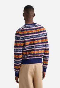 Strickpullover mit einem mehrfarbigen geometrischen Muster in Marineblau, Weiß, Gelb und Rot, mit geripptem Saum und Bündchen.