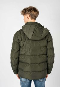 Donkergroene pufferjas met kap, met een gewatteerd textuur en een ontspannen pasvorm. Versterkte stiknaad en ritssluiting aan de voorkant.